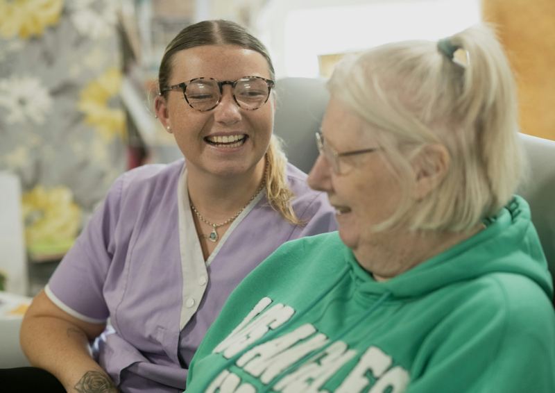 A caregiver and an older woman laughing together at home