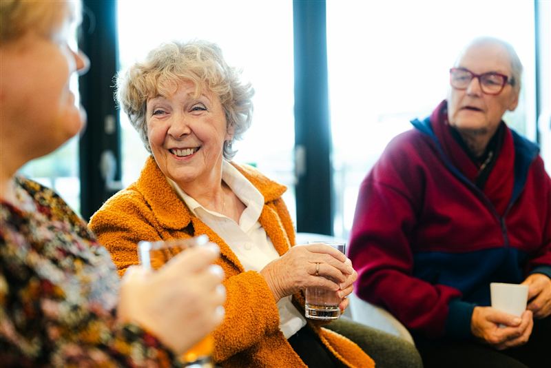 Seniors laughing together over drinks in a warmly lit room