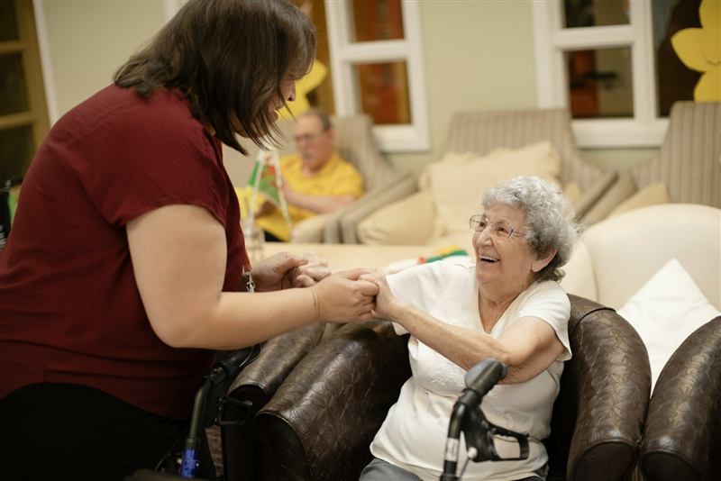 Caregiver gently helping a senior woman up from her armchair at home